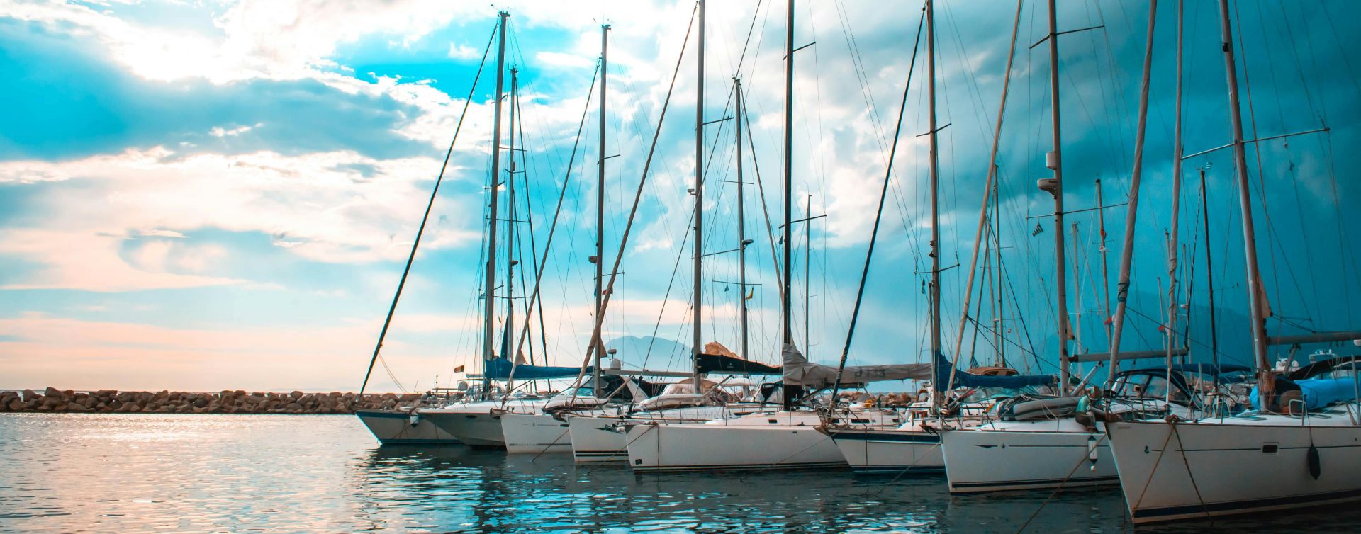 A serene scene of sailboats docked in a picturesque Patra harbour with vibrant sky reflections.