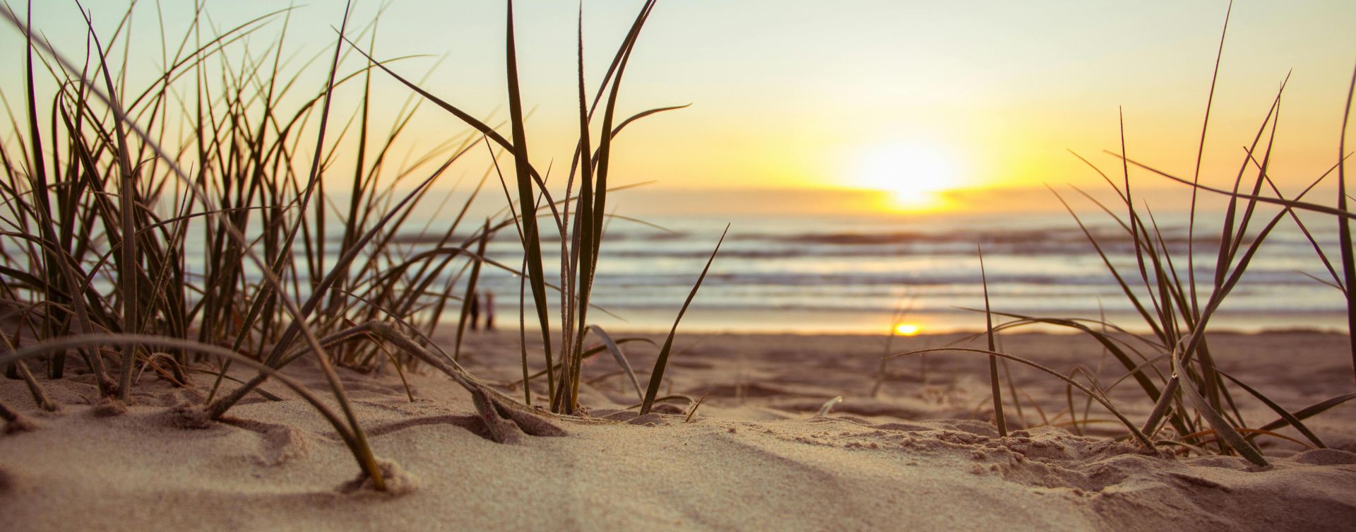 Peaceful beach scene at sunset with sun, sea, and sandy dunes in view. Ideal for nature themes.